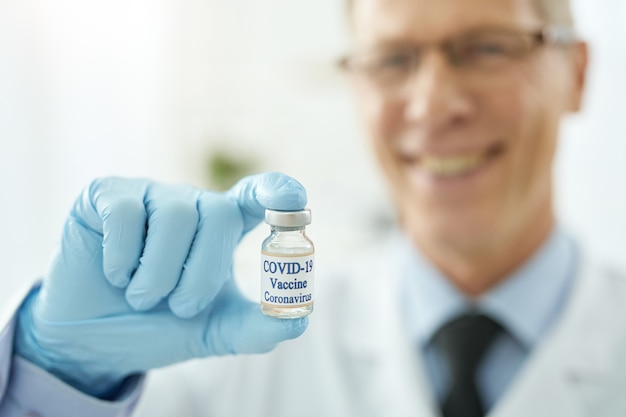 Gros plan d'un travailleur médical joyeux tenant une bouteille de vaccin contre le coronavirus. Concentrez-vous sur la main de l'homme avec un médicament