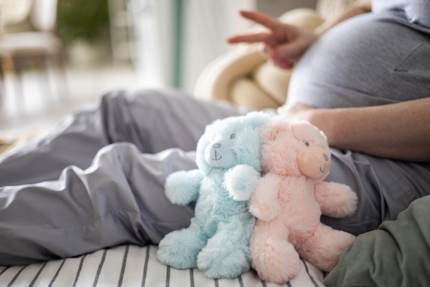 Gros plan sur le ventre d'une femme enceinte avec des jouets d'ours gesticulant deux doigts en attente de jumeaux bébé garçon et fille