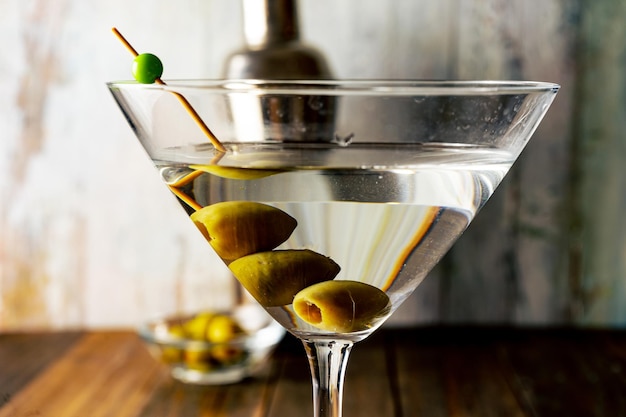 Gros plan d'un verre à martini aux olives sur fond clair.