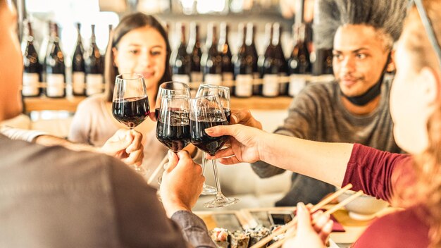 Gros plan sur des verres à boire pleins de vin rouge, des gens en arrière-plan, des amis portant un toast et tintant pour un événement de célébration