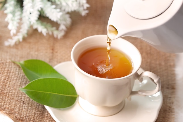Gros plan versant le thé noir chaud dans une tasse de thé blanc, concept de temps de cérémonie du thé