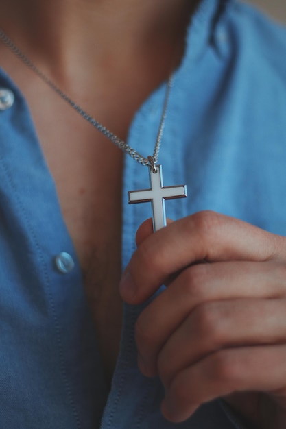 Gros plan vertical tourné d'un homme tenant un collier en argent avec un pendentif croix