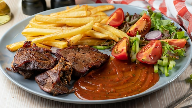 Gros plan de viande rôtie avec sauce légumes et frites dans une assiette sur la table