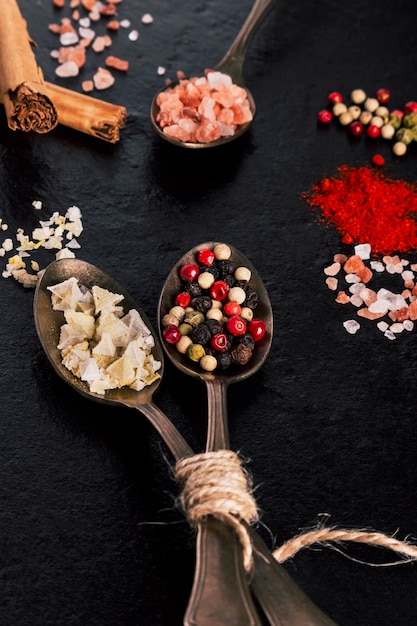 Gros plan sur des vinaigrettes traditionnelles, des cuillères avec du sel en flocons et du poivre sur fond noir