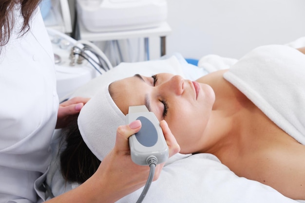 Gros plan sur le visage d'une belle femme pendant la procédure de peau par ultrasons au salon de spa Peeling du visage par ultrasons Nettoyage du visage par ultrasons en cosmétologie
