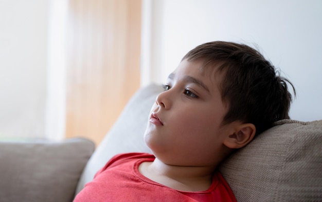 Gros plan visage enfant avec visage curieux Vue latérale Portrait Enfant assis sur un canapé regardant profondément dans ses pensées Jeune garçon mignon assis sur un canapé regardant la télévision ou se relaxant à la maison le week-end