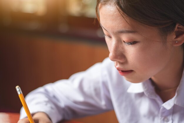 Gros plan sur le visage d'une étudiante regardant la mise au point dans un livre avec un crayon sur la table et un papier vide blanc clair orange étude et concept d'éducation espace de copie pour le texte et la conception