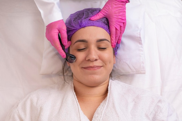 Gros plan visage féminin avec dermaroller pour les procédures de mésothérapie soins de la peau à la maison et au salon Rouleau méso avec microaiguilles