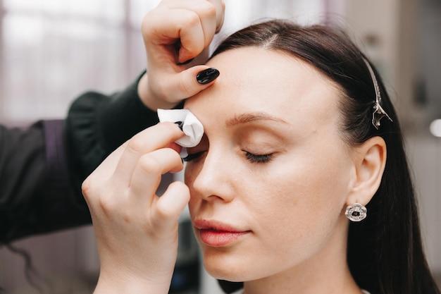 Gros plan sur le visage d'une fille Le maître tient un crayon blanc et dessine la forme des sourcils pour le maquillage permanent