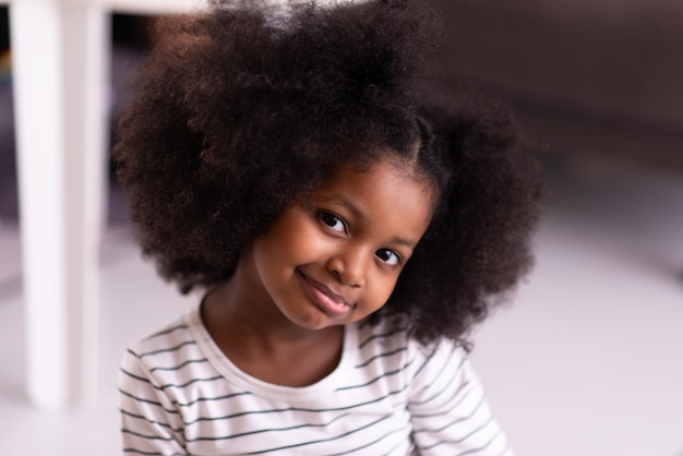 Photo gros plan sur le visage d'une jolie jeune fille africaine aux cheveux bouclés regardant vers la caméra