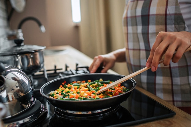 Gros plan et vue en coupe des mains de femme tenant la poêle et mélanger les aliments là-dedans.