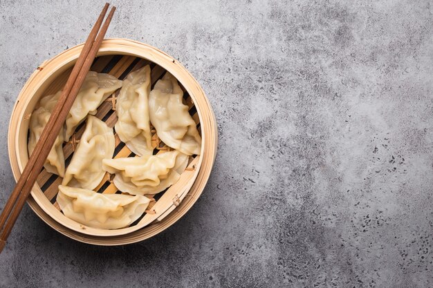 Gros plan, vue de dessus des boulettes asiatiques/chinoises traditionnelles dans un bateau à vapeur en bambou avec des baguettes sur fond de pierre rustique grise avec un espace pour le texte. Cuisine chinoise authentique, espace de copie