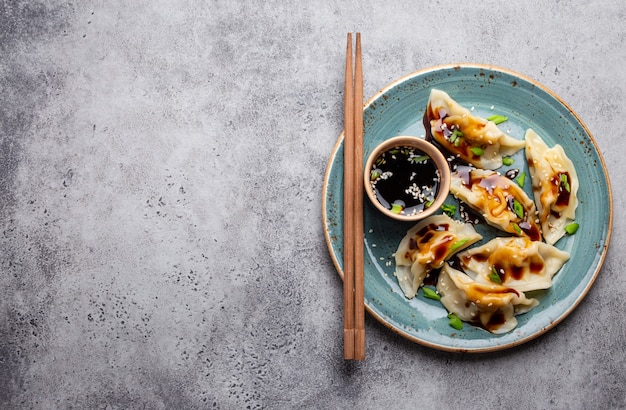 Gros plan, vue de dessus de boulettes traditionnelles asiatiques/chinoises sur une assiette bleue avec sauce soja et baguettes sur fond de pierre rustique grise avec un espace pour le texte. Cuisine chinoise authentique, espace de copie