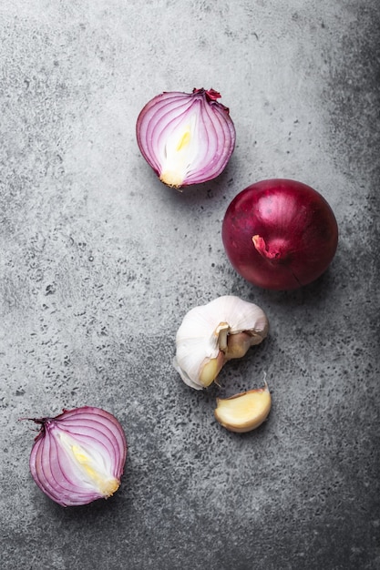 Gros plan, vue de dessus d'oignons rouges frais crus coupés et d'ail sur fond de pierre grise rustique. Cuisine, nourriture végétarienne ou concept d'alimentation saine, nourriture biologique propre