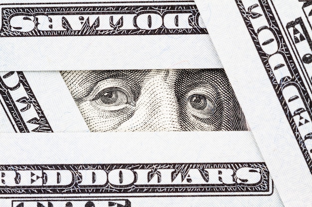 Gros plan des yeux de Benjamin Franklin entre les billets de cent dollars