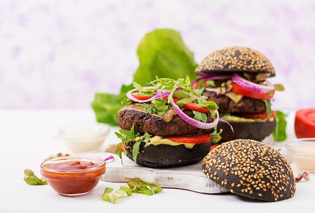 Gros sandwich noir - hamburger noir avec hamburger de boeuf juteux, fromage, tomate et oignon rouge sur une surface claire.