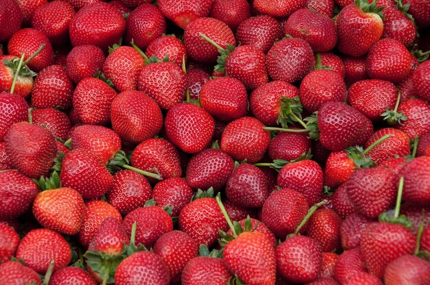 Un gros tas de fraises avec les feuilles vertes dessus.