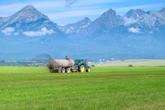 Un gros tracteur épandant de l'engrais pour améliorer la récolte sur prairie de pâturage ou champ en haute tat...