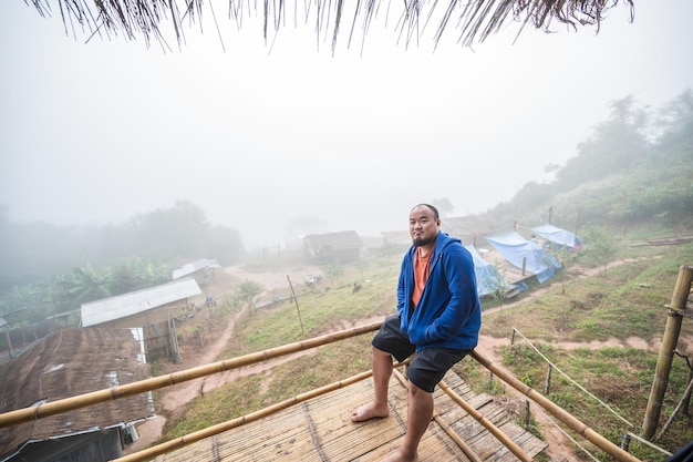 Gros voyageur asiatique assis sur le balcon en bois avec un beau paysage et de la brume le matin du village de Sapan nan ThailandSapan est un petit village tranquille dans la montagne