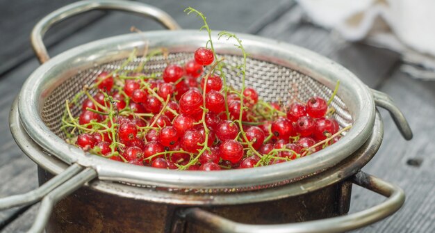 Groseille rouge dans une passoire sur une table en bois noir