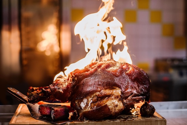 Une grosse cuisse de porc grillée avec un feu sur la cuisine professionnelle