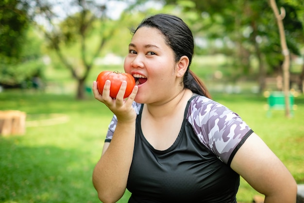 Grosse femme asiatique manger des tomates au parc naturel