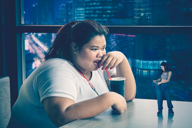 Grosse femme boit du soda en rêvant d'avoir un corps mince