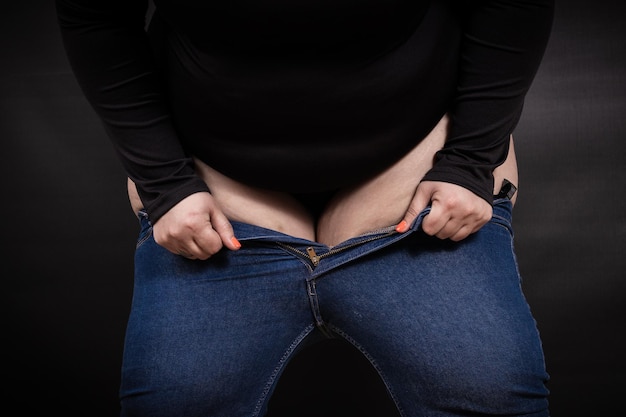 Une grosse femme met un petit jean sur elle-même sur fond noir Photo de haute qualité