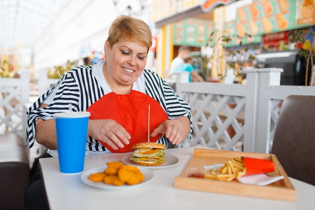 Grosse femme se prépare à manger du fast-food dans l'aire de restauration du centre commercial.