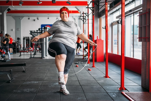 Grosse femme en sueur, faire de l'exercice avec une corde dans une salle de sport. Calories brûlées, personne de sexe féminin obèse sur une formation dans un club de sport, l'obésité