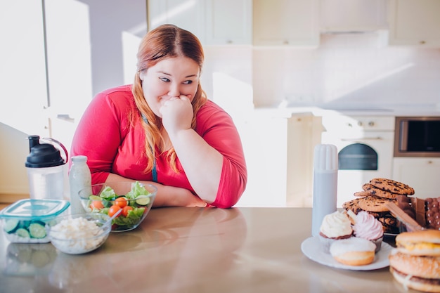 Grosse jeune femme dans la cuisine, assis et manger de la nourriture