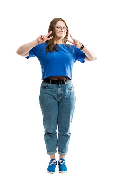 Une grosse jeune femme souriante en T-shirt bleu et jeans se dresse et montre le signe de la victoire