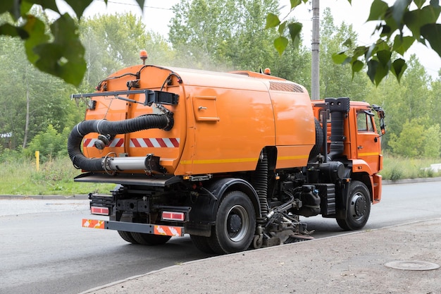 Une grosse machine orange dégage l'asphalte avec une balayeuse près du trottoir