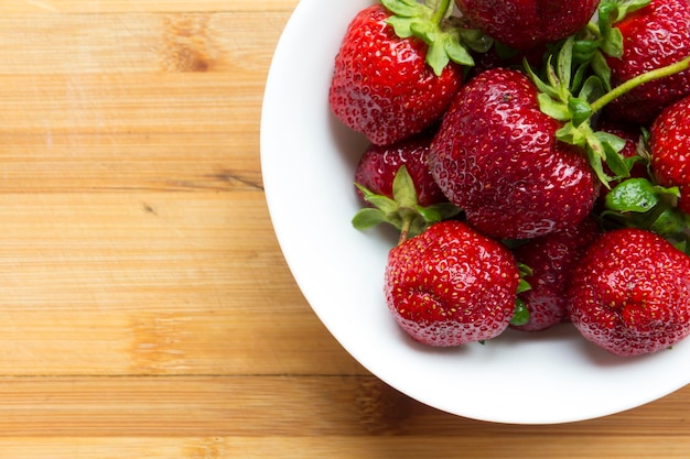 De grosses fraises rouges se trouvent dans une assiette blanche sur une surface en bois