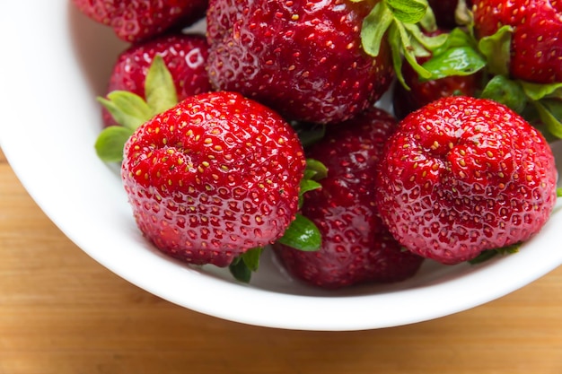 De grosses fraises rouges se trouvent dans une assiette blanche sur une surface en bois