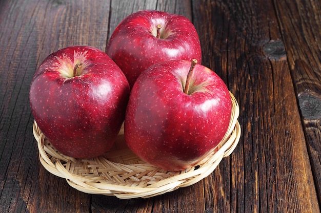 Grosses pommes rouges dans une assiette en osier sur une table en bois foncé