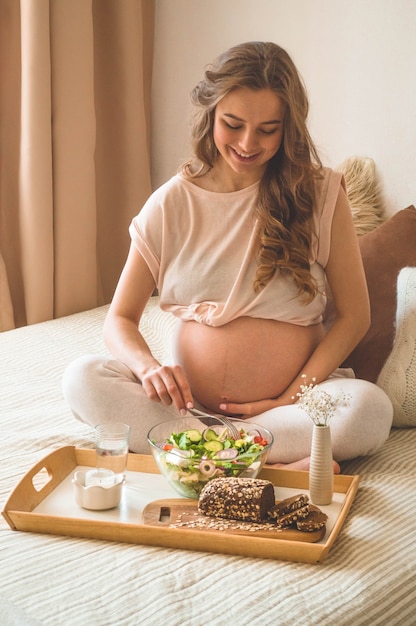 Grossesse et alimentation biologique saine. Femme enceinte bénéficiant d'une salade de légumes frais au lit, espace libre