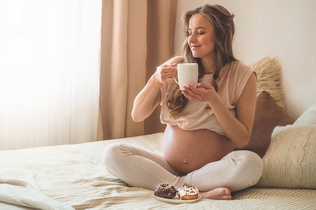 Grossesse et nutrition. Femme enceinte bénéficiant de beignets et de thé au lit, espace libre