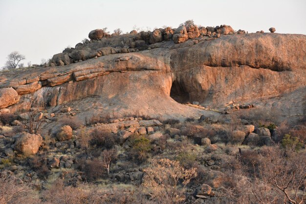 Une grotte naturelle dans une colline rocheuse Des pierres sont éparpillées sur la colline et des buissons poussent