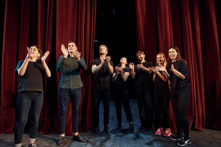 Photo un groupe d'acteurs vêtus de couleurs sombres se tiennent contre des rideaux rouges lors d'une répétition au théâtre.