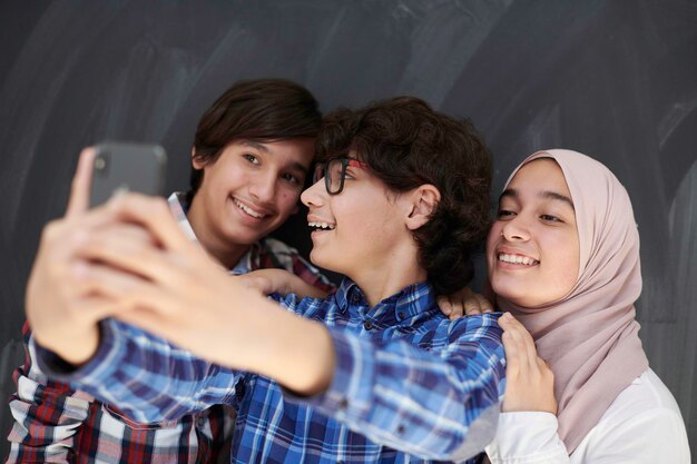 groupe d'adolescents arabes prenant une photo de selfie sur un téléphone intelligent avec un tableau noir en arrière-plan