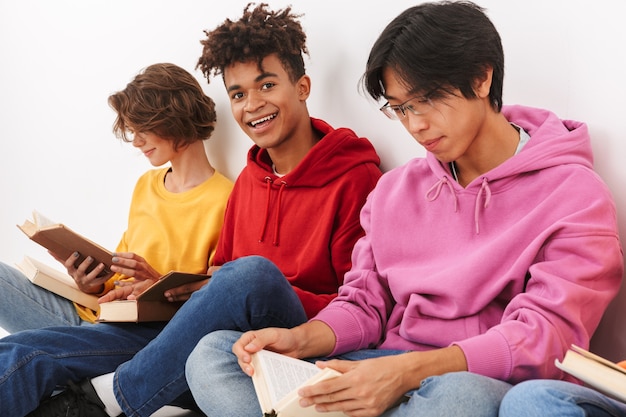 Groupe d'adolescents souriants gais isolés, lisant des livres