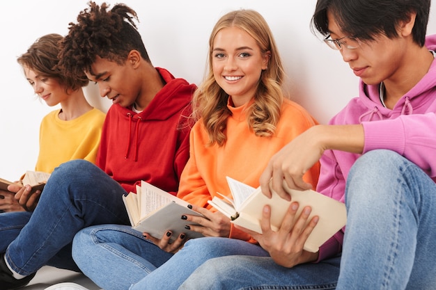 Groupe d'adolescents souriants gais isolés, lisant des livres