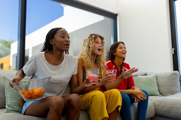 Groupe d'amies diverses et excitées, assises sur un canapé, regardant le sport à la télévision