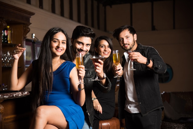 Groupe d'amis asiatiques indiens assis au bar-salon, buvant des boissons ou des cocktails, célébrant le nouvel an, un anniversaire ou un succès