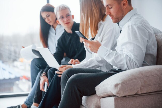 Groupe d'amis assis sur le canapé avec ordinateur portable et téléphones ensemble