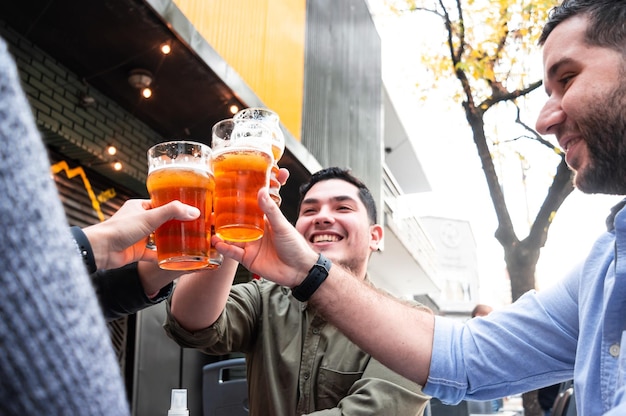 Groupe d'amis assis à l'extérieur d'un bar portant un toast et buvant de la bière