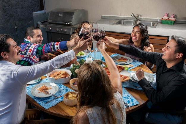 Groupe d'amis assis à une table grillant avec des verres de vin pendant le dîner de Noël