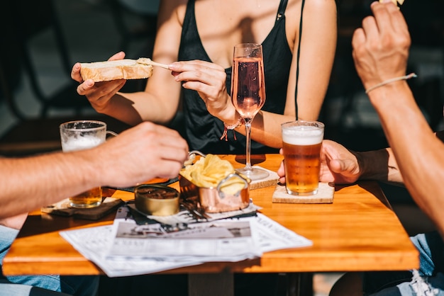 Groupe d'amis assis sur une terrasse d'été avec de la bière et du champagne dans leurs mains et des collations sur la table