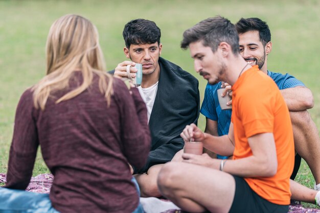 Groupe d'amis buvant du thé et parlant avec une expression détendue assis sur un parc